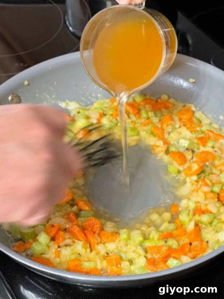 Chicken stock being slowly added and whisked into the mirepoix and roux mixture.