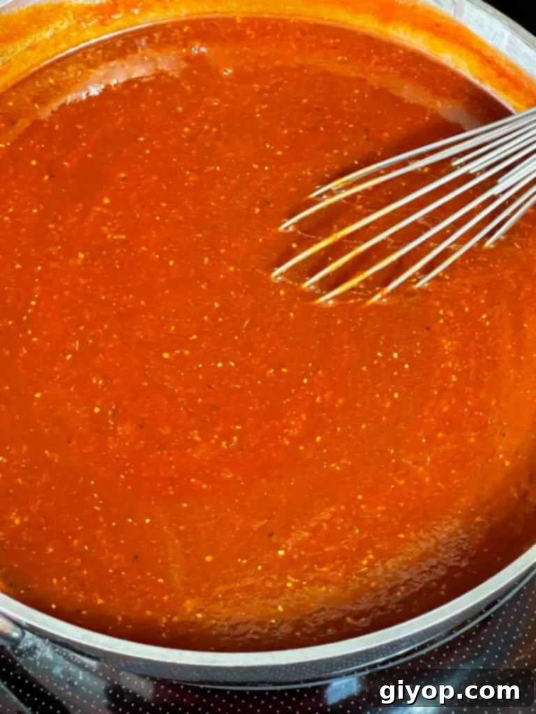 Legendary Kansas City Barbecue Sauce 6 The Kansas City style barbecue sauce is simmering gently in a saucepan, with steam rising, indicating it's cooking down.