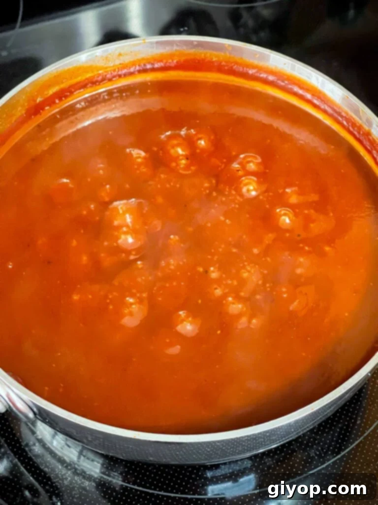 Legendary Kansas City Barbecue Sauce 7 Another view of the Kansas City style barbecue sauce gently simmering in a saucepan on the stovetop, with a spatula resting nearby.