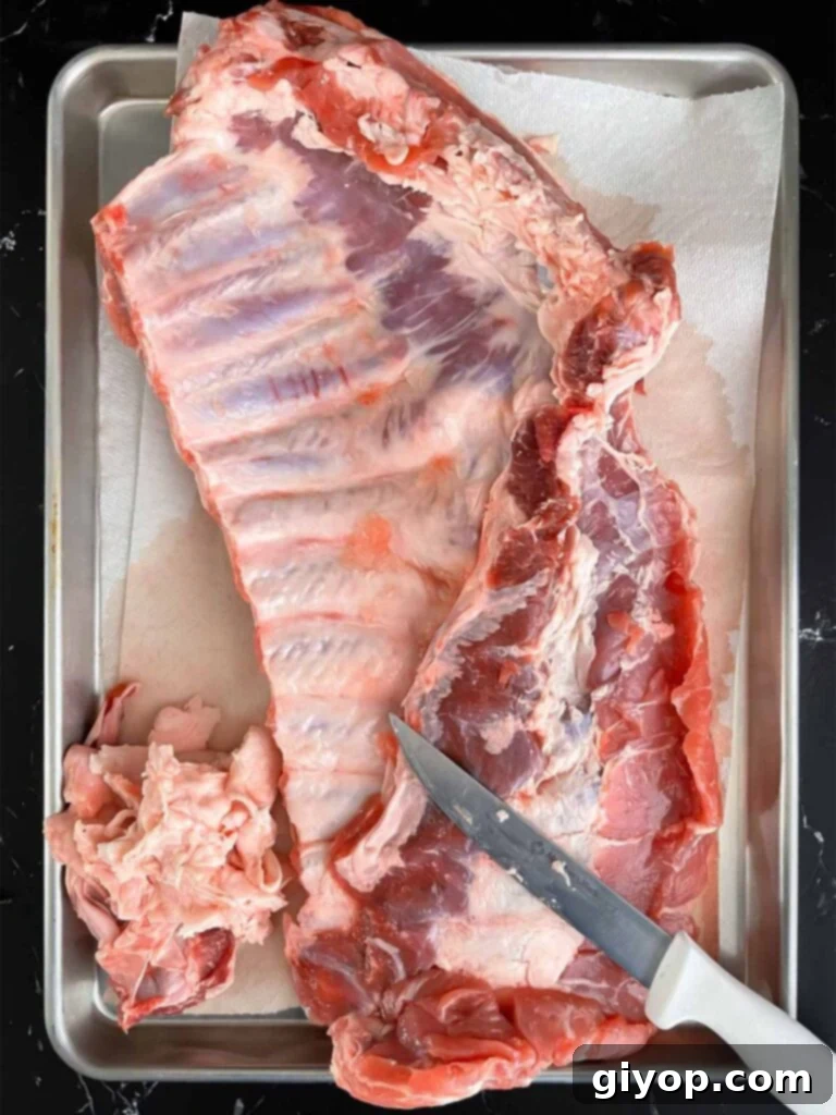A rack of spareribs on a baking sheet being trimmed to prepare for smoking.