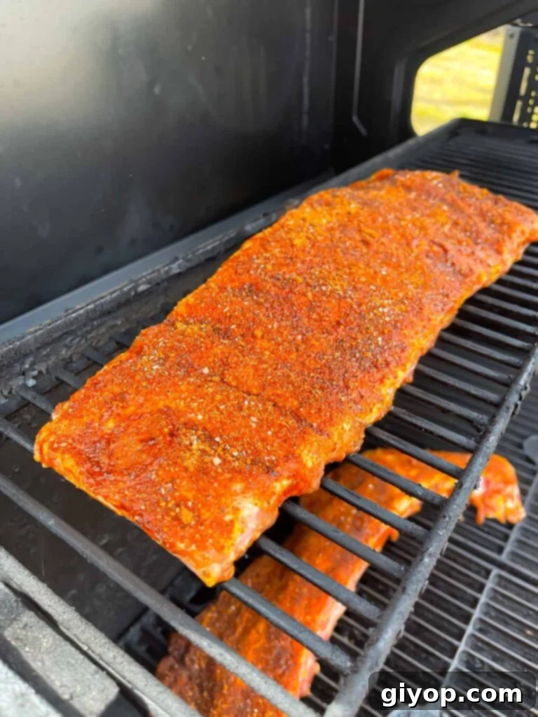 Kansas City style ribs smoking on a grill, developing a rich, dark bark.