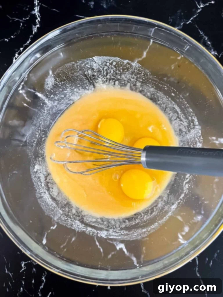 Eggs being added to a sugar butter mixture in a glass bowl.