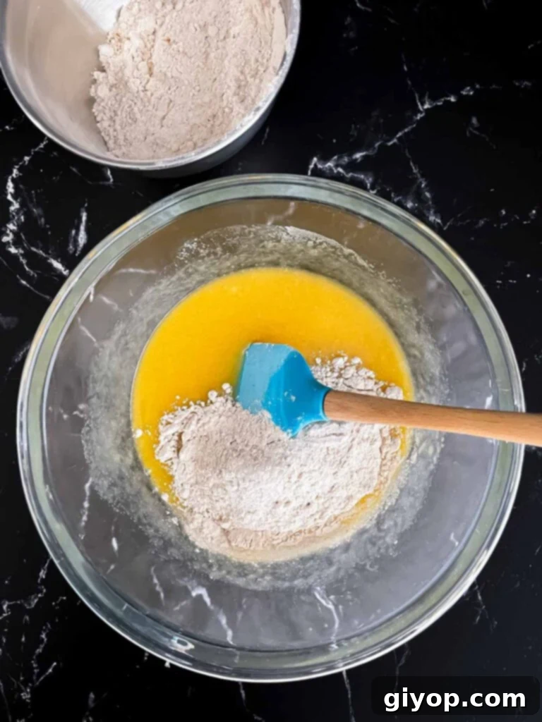 Flour being added to a butter egg mixture in a glass bowl.