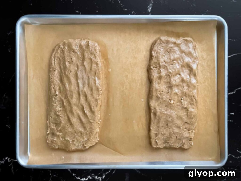 Chai biscotti dough shaped into loaves on a baking sheet, ready for the first bake.