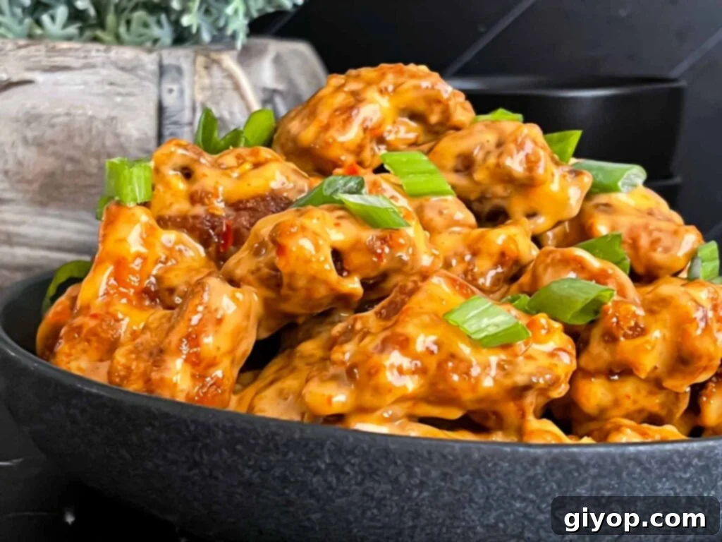 A bowl of crispy Bang Bang Chicken, generously coated in creamy orange sauce and garnished with fresh green onions.