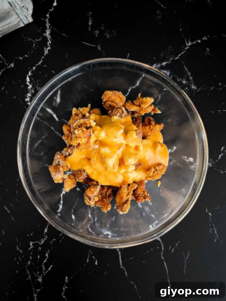 Crispy fried chicken being tossed with creamy Bang Bang sauce in a large clear glass bowl.