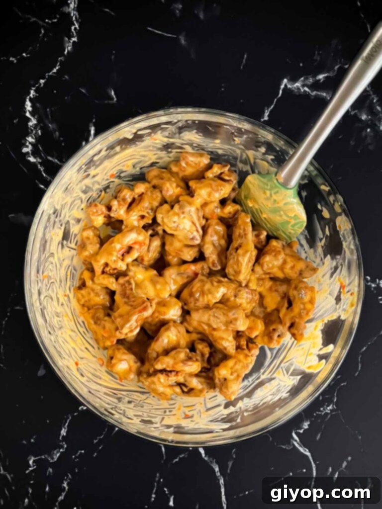 More crispy fried chicken being mixed thoroughly with the creamy Bang Bang sauce in a large glass bowl, ensuring complete coverage.
