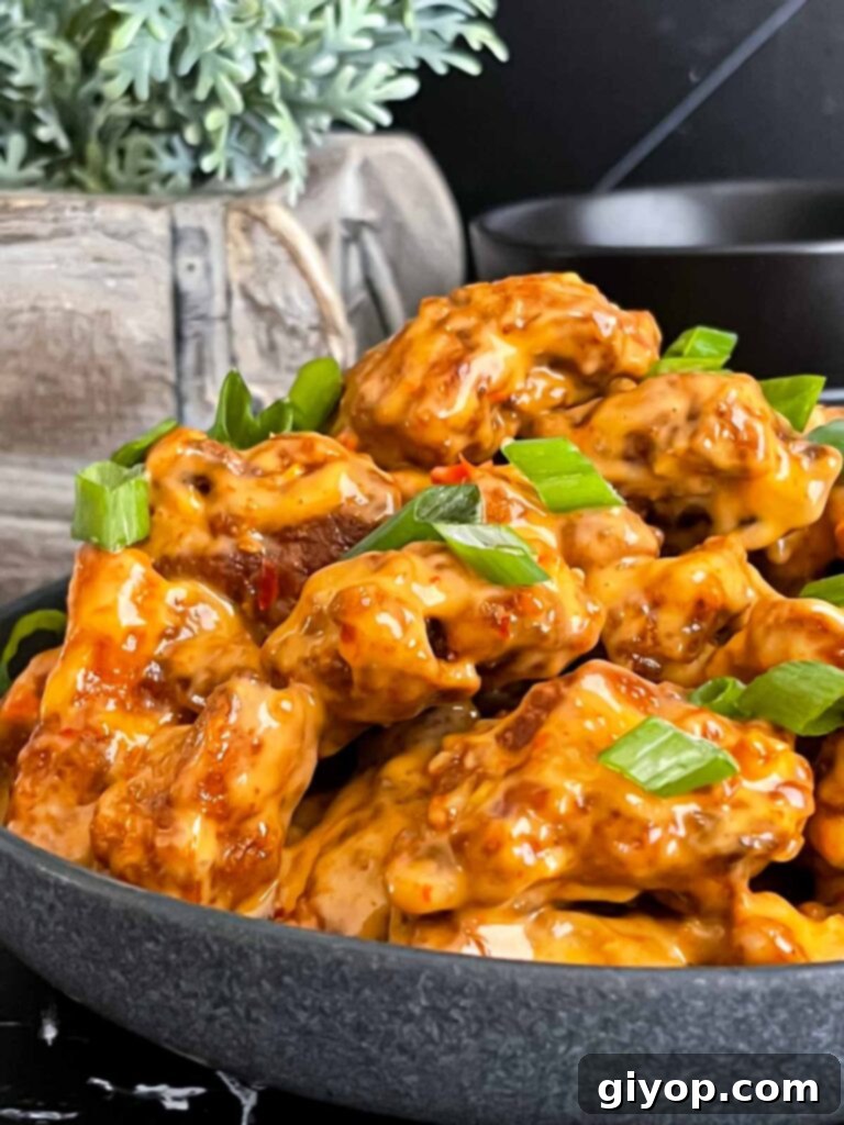 A dark serving bowl filled with Bang Bang Chicken, garnished generously with vibrant green onions.