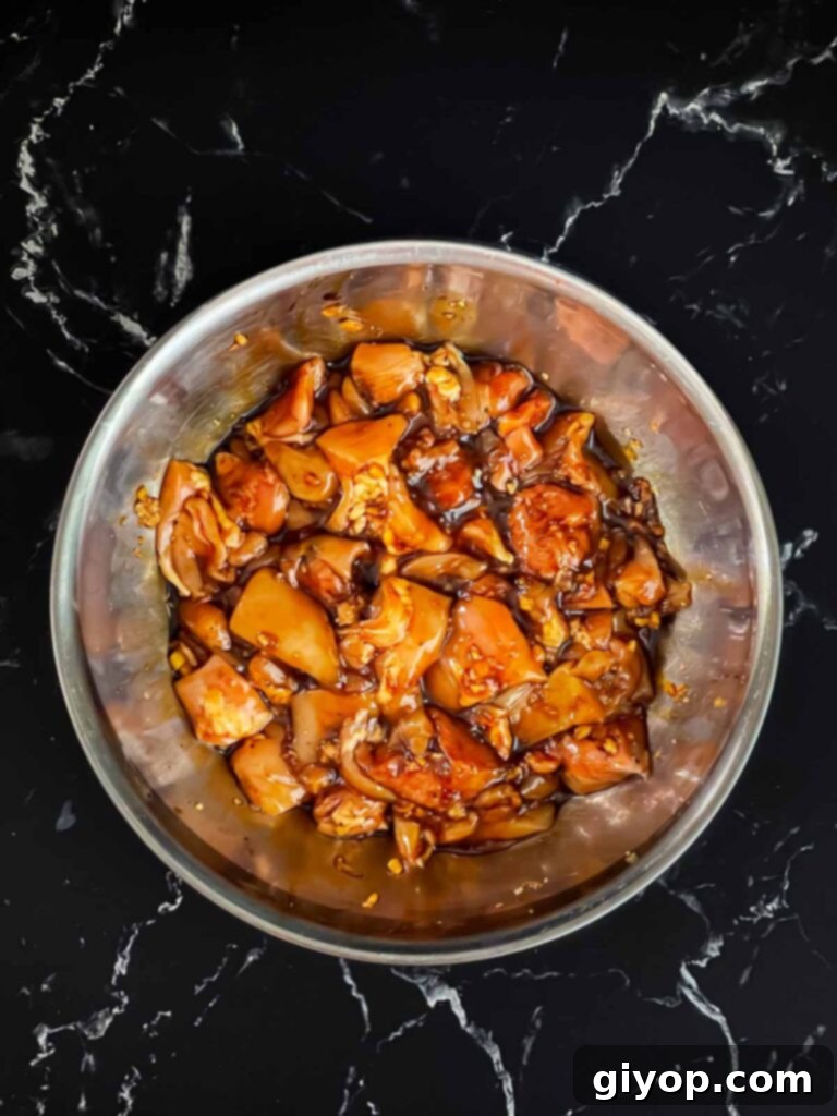 Bite-sized chicken pieces fully coated in a rich, dark marinade within a glass bowl.