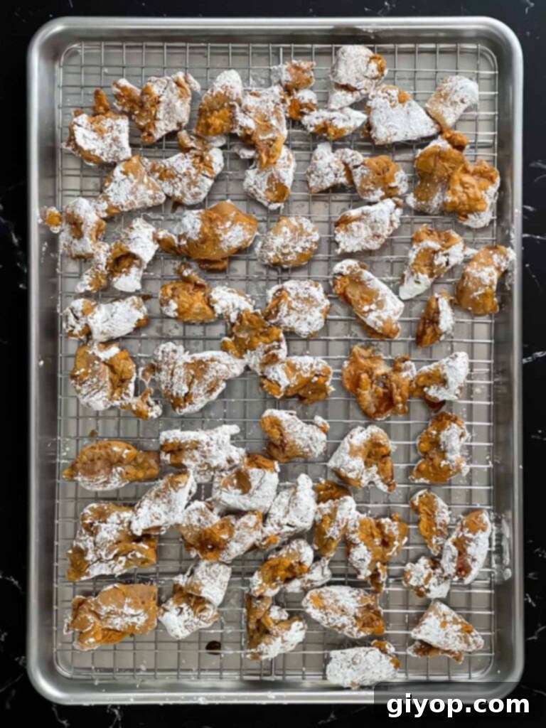 Bite-sized marinated chicken pieces being thoroughly coated with white cornstarch in a bowl.