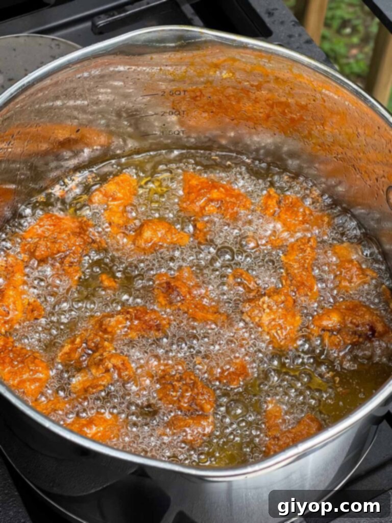 Several pieces of bite-sized chicken frying in hot oil in a large pan, turning golden brown.