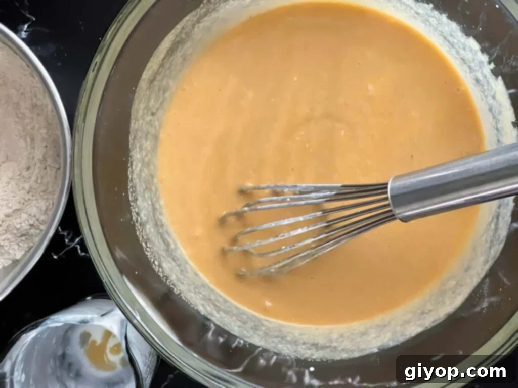 The fully combined wet ingredients—sugar, eggs, melted butter, buttermilk, and vanilla extract—swirl together in a large glass bowl.
