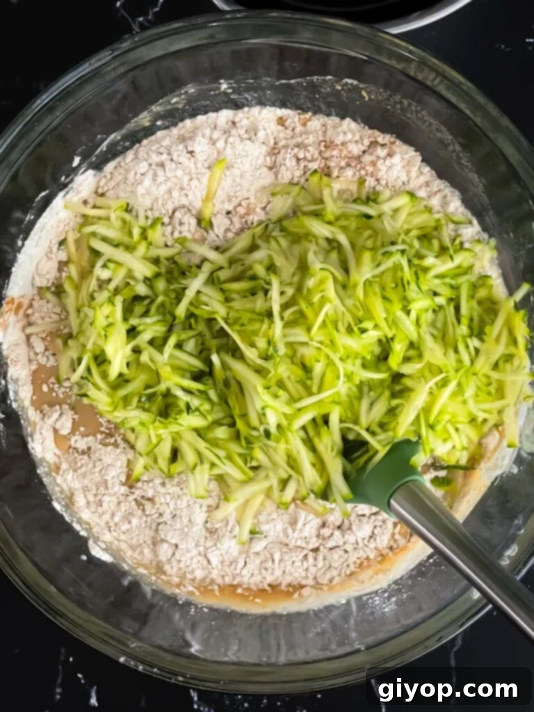 Freshly grated zucchini is carefully folded into the muffin batter, adding natural moisture and a delicate texture to the mix.