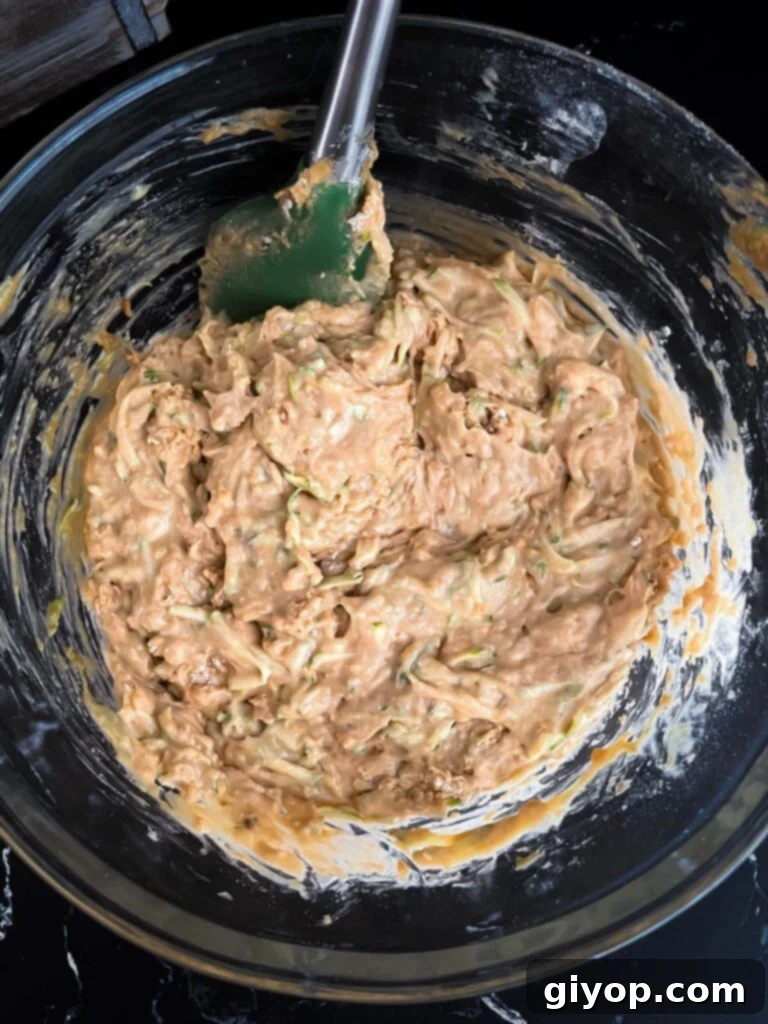 The finished zucchini muffin batter, thick and speckled with green zucchini shreds, rests in a large glass bowl, ready for baking.