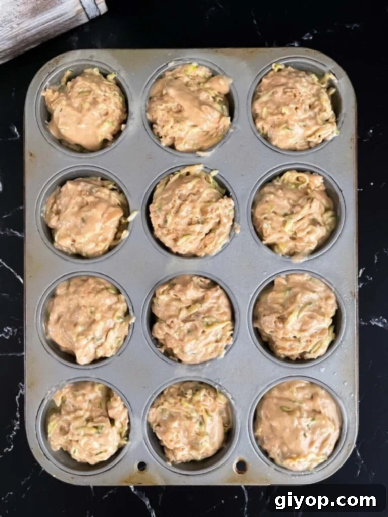 Unbaked zucchini muffin batter, portioned perfectly into a baking tin lined with paper cups, ready to go into the oven.