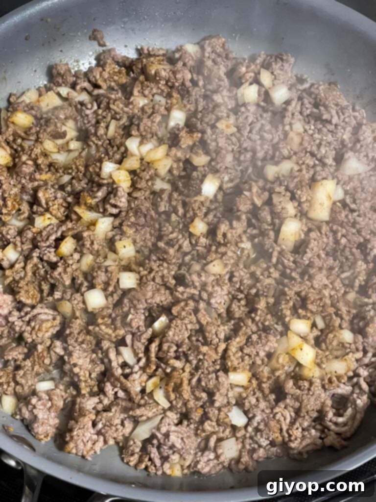 Diced onions and aromatic spices mixed with browned ground beef in a skillet, building complex flavors.