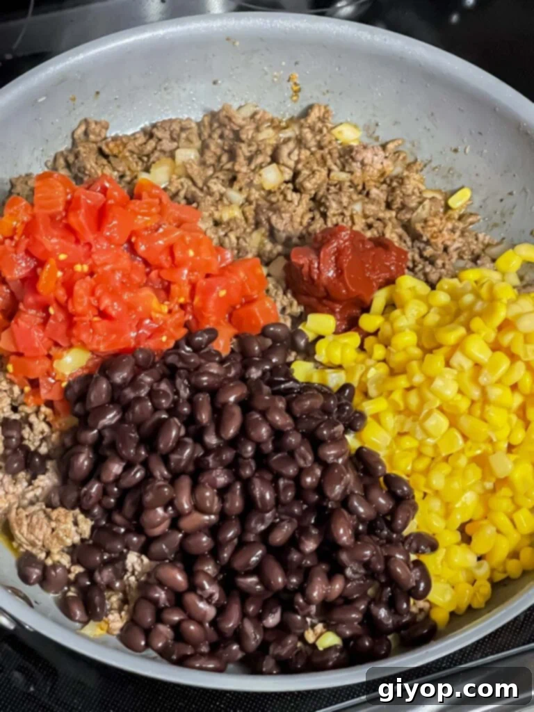Fresh vegetables, including corn and black beans, along with tomato paste, added to the seasoned ground beef in a skillet.