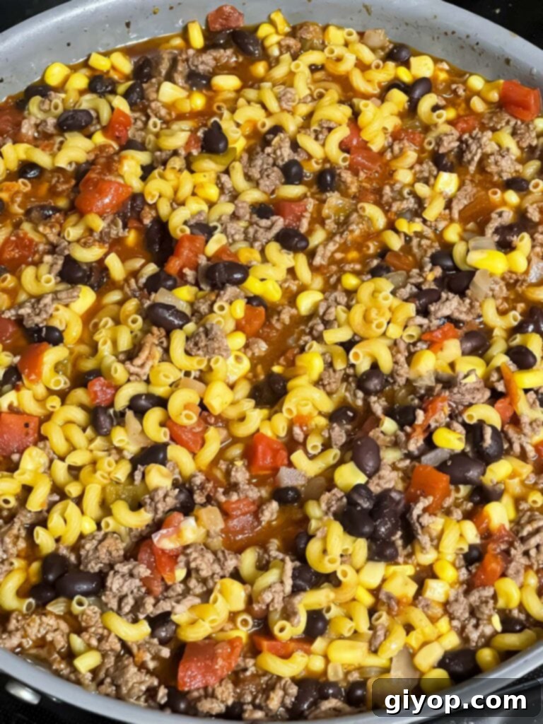 Uncooked pasta and chicken broth added to the skillet, ready to cook down into a creamy taco pasta.