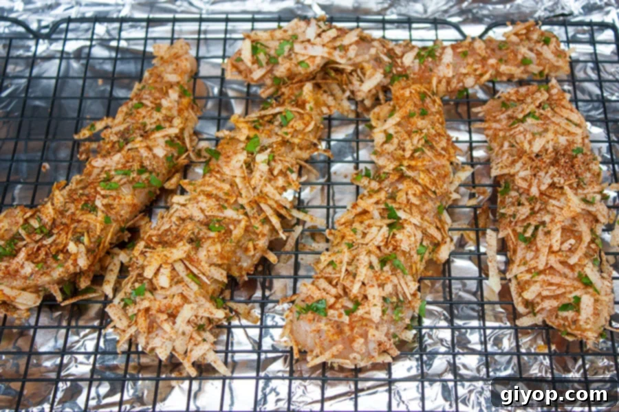 Grain-Free Parmesan Crusted Chicken Tenders 4 Unbaked Parmesan crusted chicken tenders neatly arranged on a wire rack over a foil-lined baking sheet, ready for the oven.