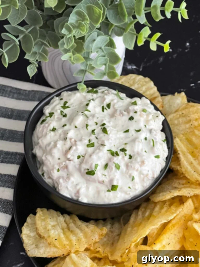 Creamy clam dip in a dark serving bowl, surrounded by a generous scattering of crispy kettle potato chips, ready for dipping.