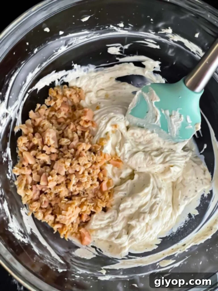 Clam dip ingredients in a glass mixing bowl with the minced clams on top, before being fully mixed.