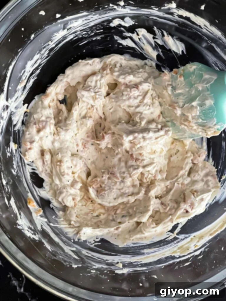 Clam dip recipe ingredients mixed together in a glass mixing bowl, showcasing the creamy texture and bits of clams.