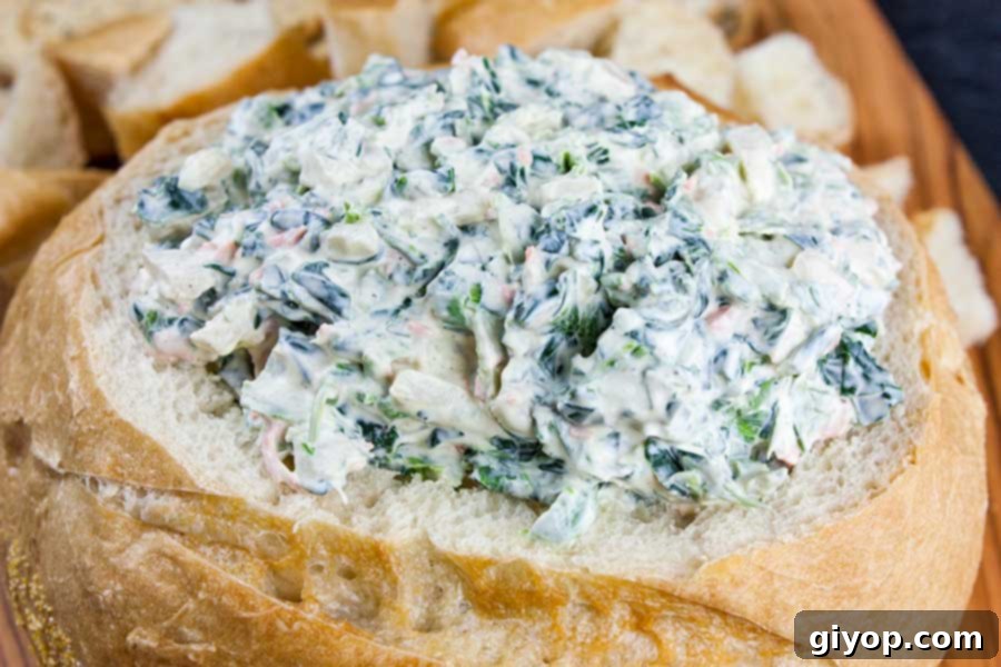 Easy spinach dip in a hollowed-out bread bowl surrounded by bread cubes for dipping.