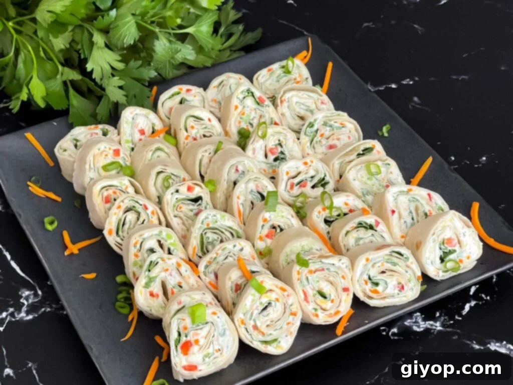 Colorful veggie tortilla roll ups arranged neatly on a square dark plate, garnished with fresh green onions and shredded carrots for a vibrant presentation.