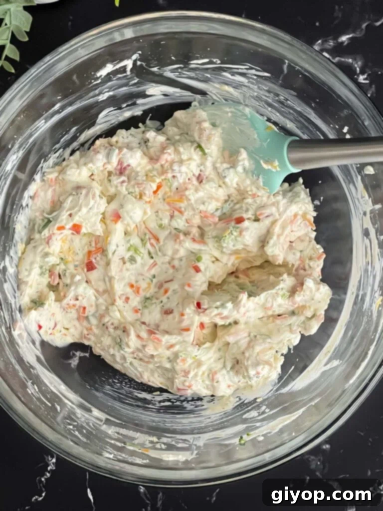 A vibrant vegetable cream cheese mixture, combined in a glass mixing bowl, for the delicious veggie tortilla roll ups.