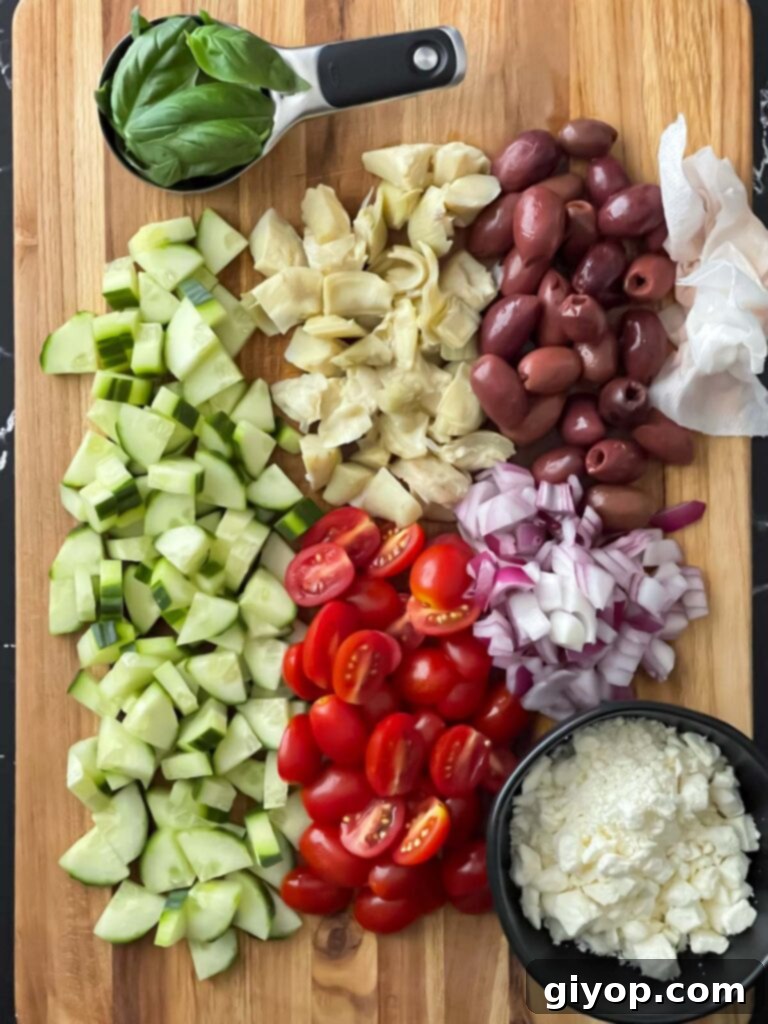Zesty Greek Tortellini Pasta Salad 6 Assortment of freshly chopped vegetables, including cucumber, tomatoes, red onion, olives, and artichoke hearts, on a wooden cutting board.