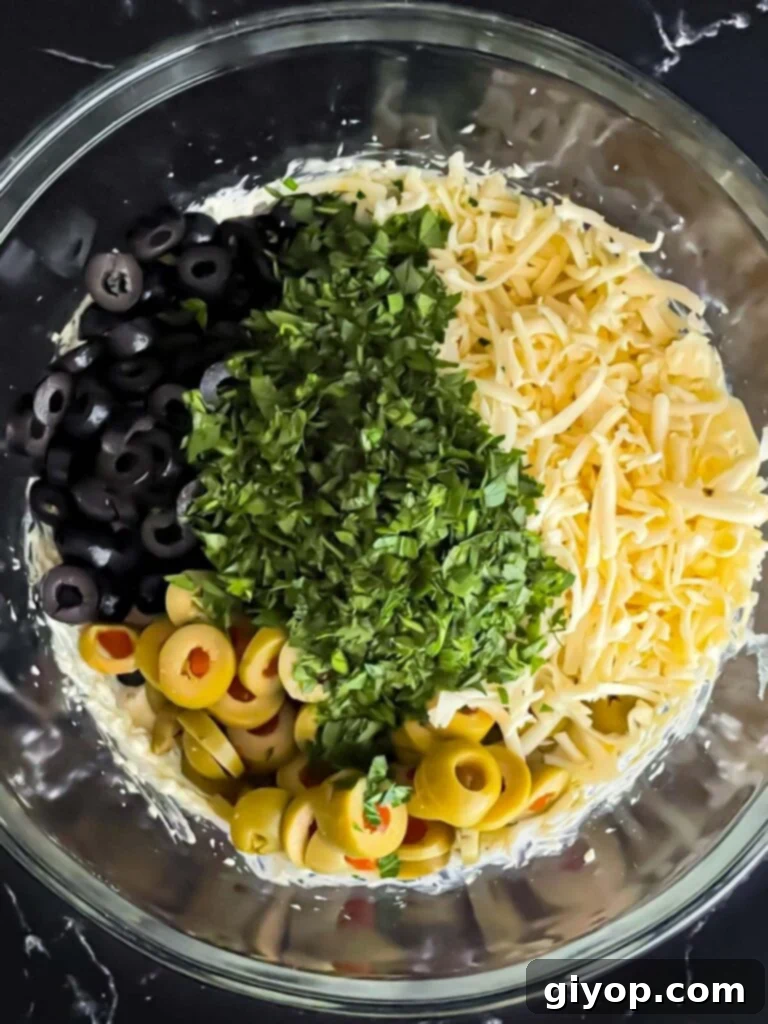 Softened butter, mayonnaise, and seasonings being thoroughly mixed in a clear glass bowl, creating a smooth base.