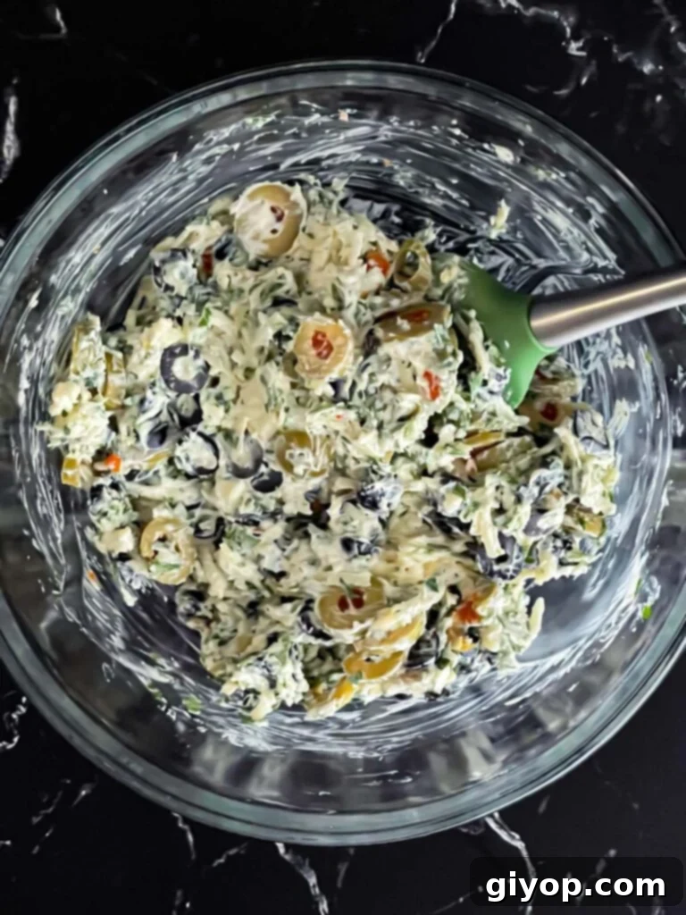 The savory olive and cheese mixture, perfectly combined in a glass bowl, showcasing the vibrant colors and textures, ready for spreading.