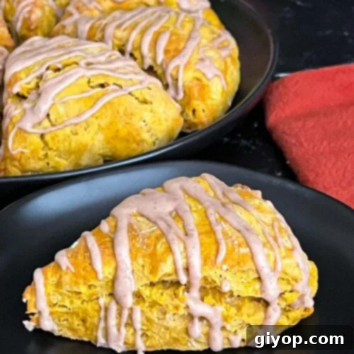 Pumpkin scones on a dark plate, indicating a finished, glazed product.