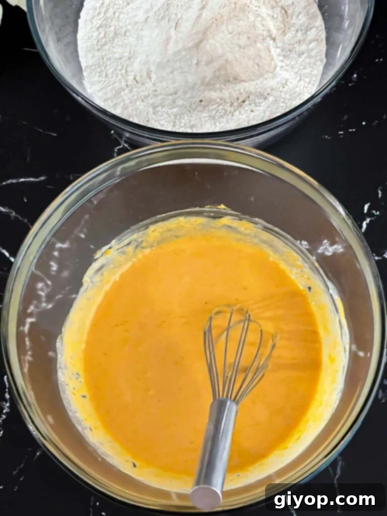Dry ingredients in a dark bowl and wet ingredients, including pumpkin puree and eggs, in a glass mixing bowl, both ready on a dark surface.