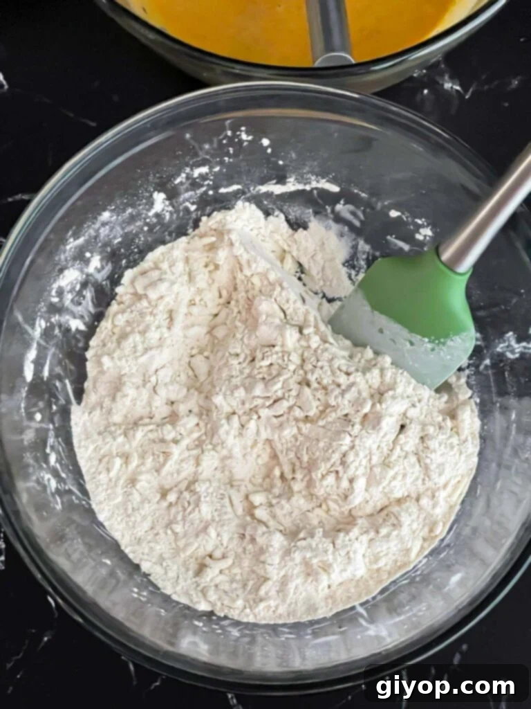 Shredded frozen butter being added to the dry ingredients in a glass mixing bowl, ensuring even coating for flaky scones.