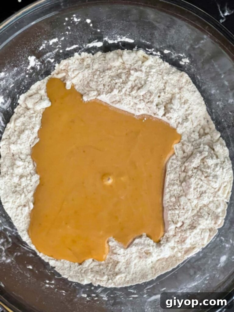 The pumpkin scone wet batter carefully poured into a well made in the center of the dry ingredients in a glass bowl.