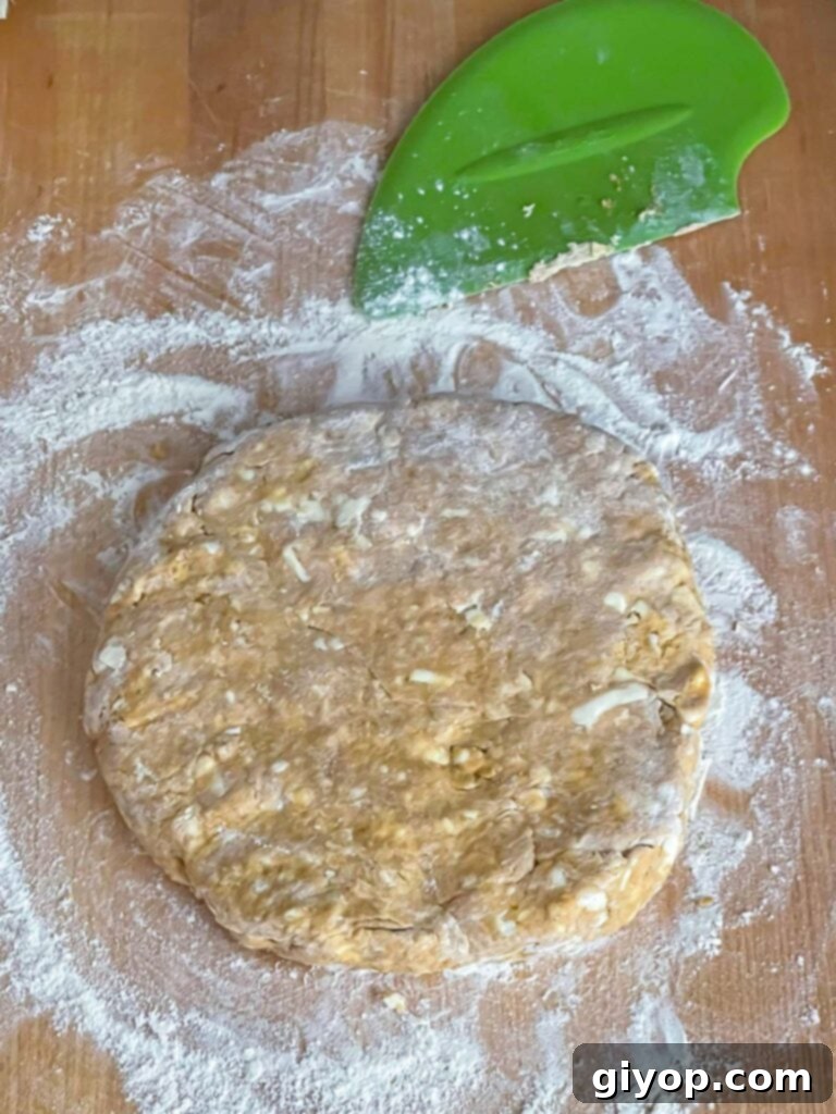 Pumpkin scone dough gently shaped into a 1-inch thick circle on a lightly floured wooden board, ready for cutting.