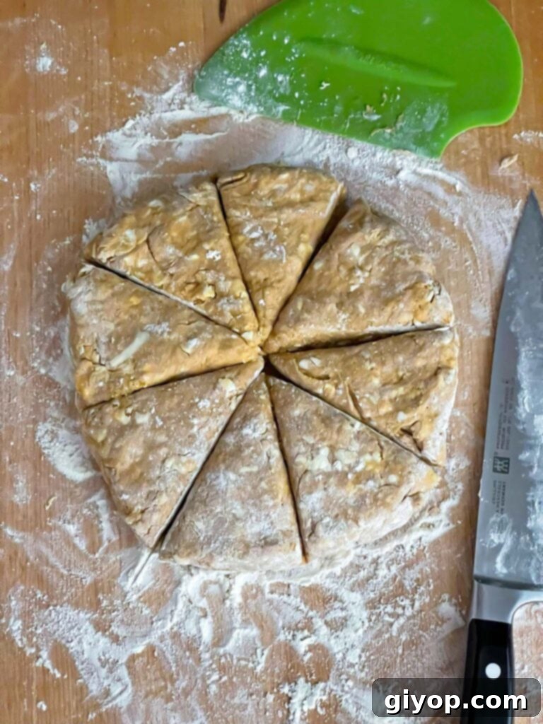 Pumpkin scone dough neatly cut into eight equal triangular pieces on a wooden board, demonstrating the precise cuts.