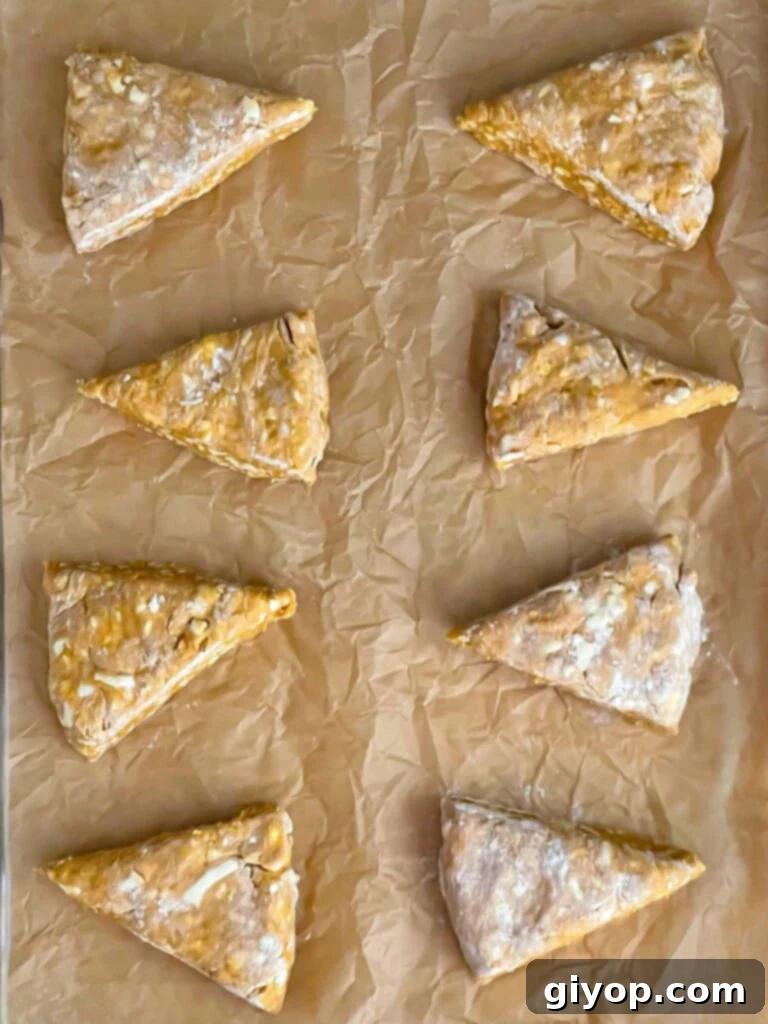 Unbaked pumpkin scones meticulously arranged on a parchment paper-lined baking sheet, ready for the oven.
