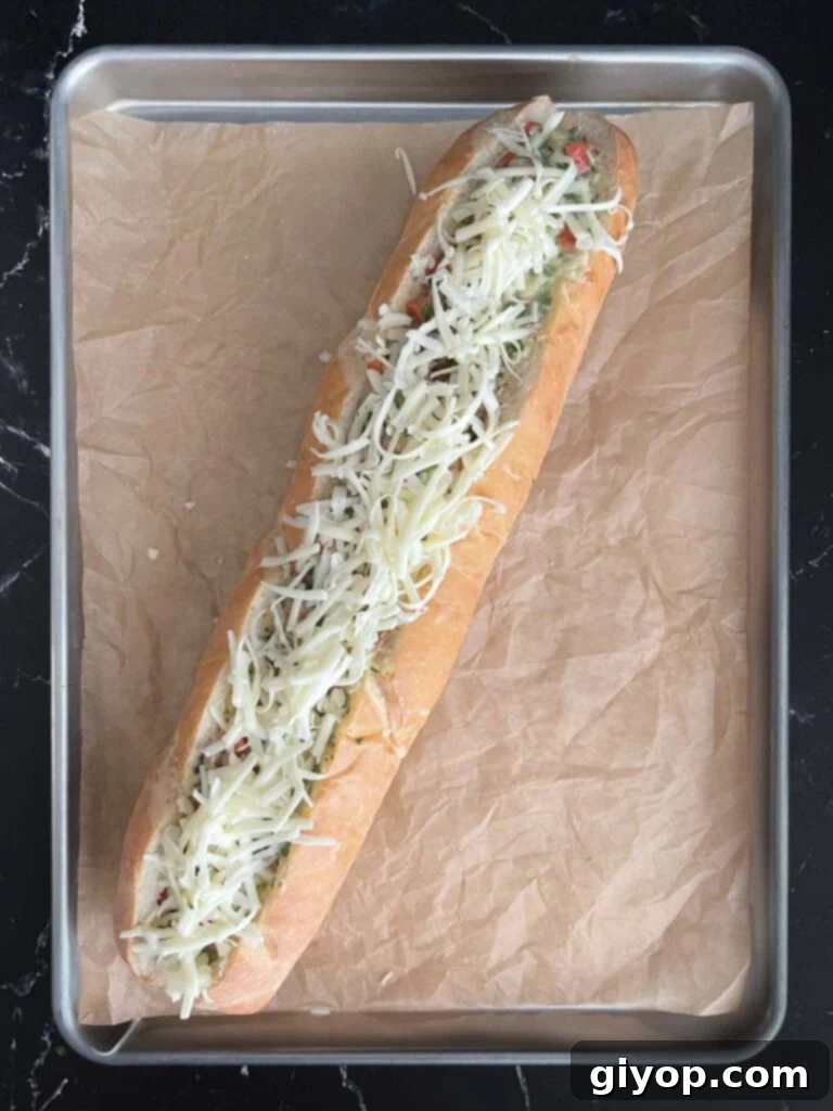 A hollowed-out French bread loaf filled with the egg mixture and topped with extra cheese, ready for baking.