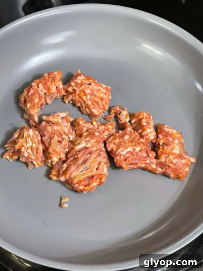 Ground Italian sausage browning in a skillet over medium-high heat.