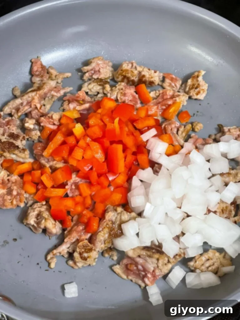 Sausage, red bell pepper, and onions cooking together in a skillet, softened and fragrant.