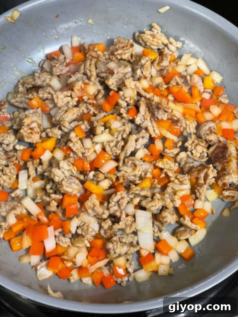 A close-up of browned sausage, red bell pepper, and onions cooking in a skillet, ready to be removed from heat.