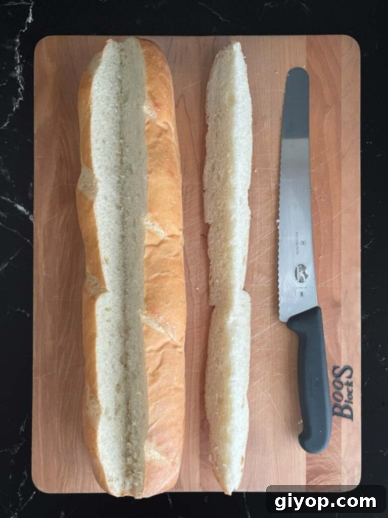 A French bread loaf on a cutting board with a V-shaped slit cut along the top, ready for hollowing.