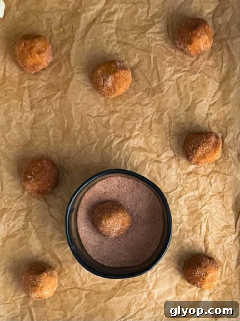 Uniformly sized Pumpkin Snickerdoodle cookie dough balls, generously coated in cinnamon sugar, arranged on a parchment paper lined cookie sheet, ready for baking.
