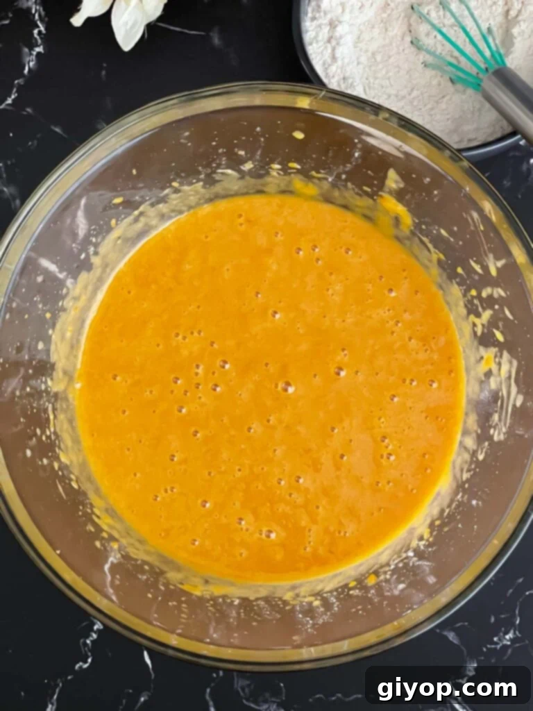 Wet ingredients for sweet potato bread recipe mixed in a glass bowl, a smooth orange batter.