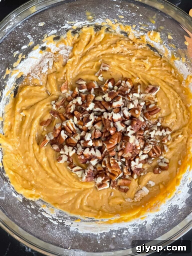 Pecans added to sweet potato bread batter in a glass bowl, ready for folding.