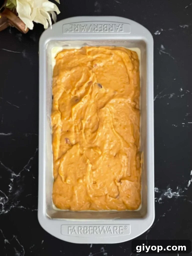 Sweet potato bread batter in a greased loaf pan on a dark surface, ready for the oven.