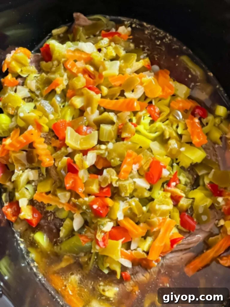 Pepperoncini and giardiniera layered over the seasoned beef in the slow cooker, ready for cooking.