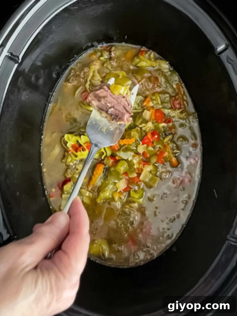 Slow-cooked Italian beef, submerged in its flavorful juices inside the slow cooker, appearing tender.